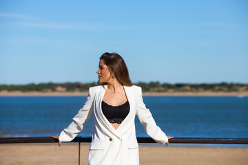 Young and beautiful blonde woman is leaning on the railing of the promenade at the mouth of the river, the woman looks to the side. In the background the blue sea.