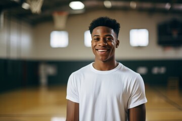Smiling portrait of a teenage male African American basketball player wearing a white t shirt in an indoor basketball gym