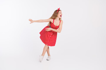 Charming retro inspired young woman in a red polka dot dress posing joyfully against a white...
