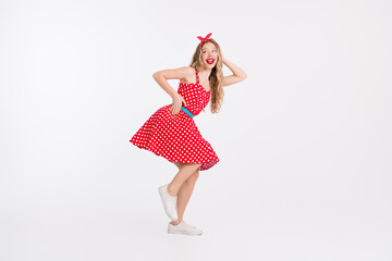 Retro inspired young woman in a red polka dot dress striking a playful and cheerful pose with a white background.