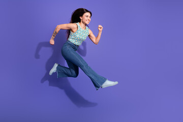 Young woman jumping in vibrant purple background showcasing energy, fashion, and positivity in casual attire.