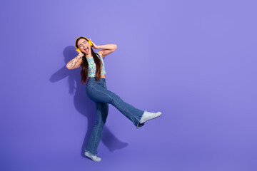 Cheerful young woman in stylish outfit enjoying music with headphones against vibrant purple background