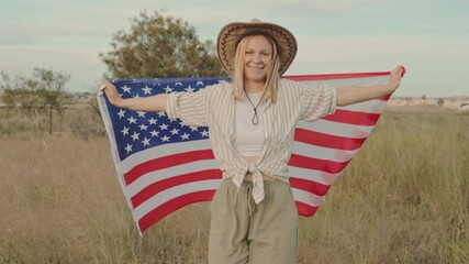 Female rancher wearing straw hat, standing in meadow, proudly waving national banner under bright sunlight, embodying rural american spirit.Usa celebrate 4th of july. Independence day concept
