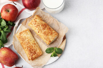 Tasty apple strudels, mint, fruits and milk on light table, flat lay. Space for text
