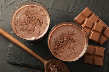 Tasty chocolate milk with shavings and pieces on black table, flat lay