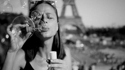 Young woman blowing soap bubbles with Eiffel Tower blurred in background, Paris, France