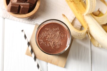 Tasty chocolate milk in glass, banana and pieces on white wooden table, flat lay