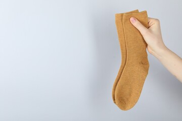 Woman with pair of socks on light grey background, closeup. Space for text