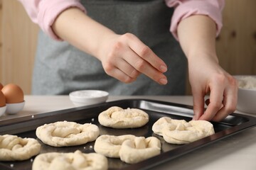 Woman putting salt onto raw pretzels at white wooden table, closeup