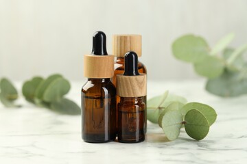 Bottles of essential oil and eucalyptus leaves on white marble table