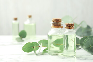 Bottles of essential oil and eucalyptus leaves on white marble table, closeup