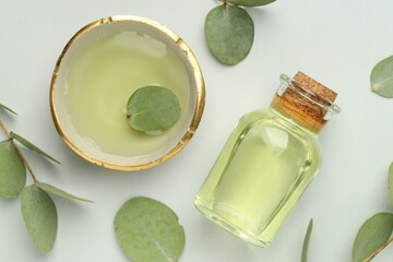 Bottle of essential oil, bowl and eucalyptus leaves on white background, flat lay