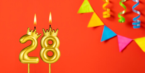 Number 28 birthday candle on an orange background with pennants
