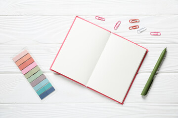 Pen, open notebook, paper clips and colorful stickers on white wooden table, flat lay