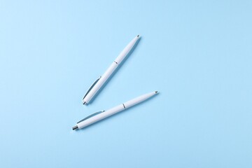 Stylish pens on light blue background, top view