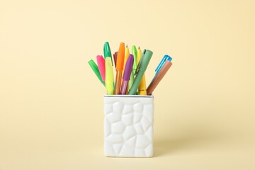 Ballpoint pens in holder on beige background, closeup