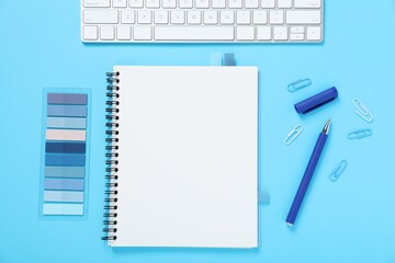 Pen, notebook, colorful stickers, paper clips and computer keyboard on light blue background, flat lay