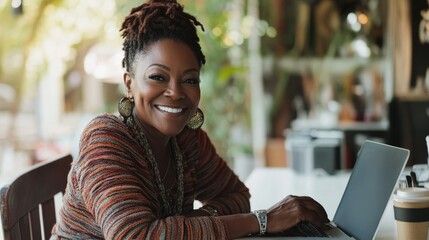 A thoughtful older woman with long, dark dreadlocks sits at a dining table, resting her chin on her hand and gazing upward, smiling slightly.