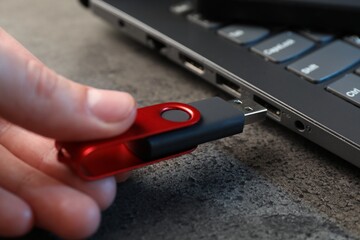 Man inserting modern flash drive at grey table, closeup