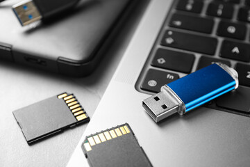 Flash drive, SD memory cards, external hard disk and laptop on light grey table, closeup