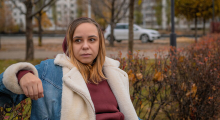 A woman sitting thoughtfully on a park bench surrounded by autumn foliage in an urban setting...