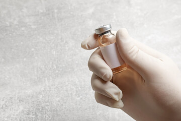 Doctor holding glass vial with hepatitis vaccine at grey table, closeup. Space for text