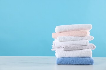 Stack of clean towels on white marble table against light blue background, space for text