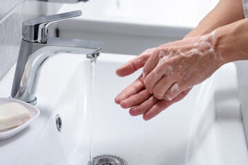 Woman washing her hands with foaming soap above sink in bathroom, closeup