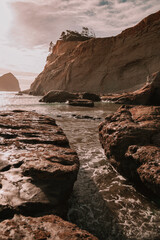 Pacific Northwest cliffside beach in late afternoon sunlight looking up at the cliffs. Oregon beach with rolling waves and sand. Ocean landscape, background, wallpaper
