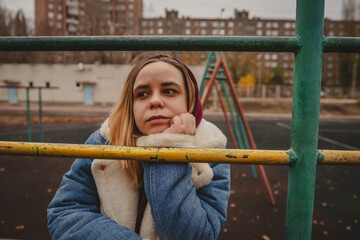Obraz premium Young woman sitting pensively at a playground during chilly autumn while wearing a hoodie and denim jacket