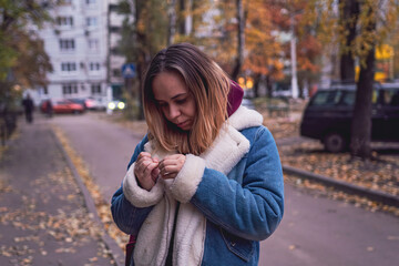 Fototapeta premium A woman stands thoughtfully in an urban setting during autumn, surrounded by trees and parked cars in a quiet neighborhood