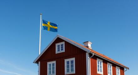 Traditional red Swedish cabin Stuga with national flag against blue sky. Close up of typical Swedish summer house architecture. National day in Sweden. 6th June.