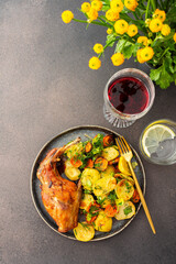 A hearty delicious dinner, baked rabbit with potatoes and carrots, a set table with food, a glass of wine and a vase of flowers