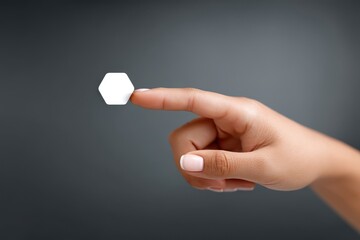 A close-up shot of a human hand with a neatly manicured index finger touching a small, white hexagonal shape. The background is gradient gray, creating a minimalist and modern aesthetic. 