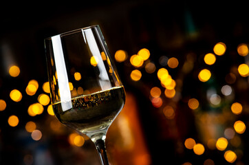 White Chardonnay wine glass and wine bottles on dark bar background with lights