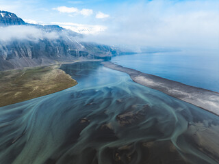 Aerial view of glacial river delta flowing into the sea, with surreal turquoise patterns and coastal cliffs in Iceland.