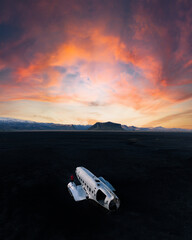 Aerial view of the DC-3 plane wreck on Solheimasandur’s black sand with a fiery sunrise sky and a solitary figure in red creating a striking contrast.