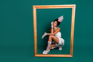 Elegant young woman in an ornate costume posing inside a golden frame against a green backdrop