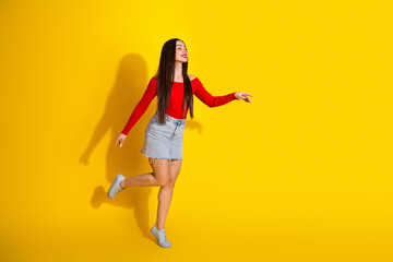 Young woman in red shirt and denim skirt posing joyfully against a vivid yellow background, expressing energy