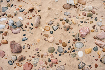 Colorful sea pebbles scattered across the sandy shore. Natural beach texture background with various shapes and stones.