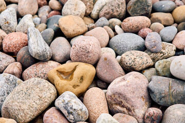 Close-up view of colorful wet pebbles on a sandy beach. One light brown stone with a water-filled hole stands out among the naturally polished stones.