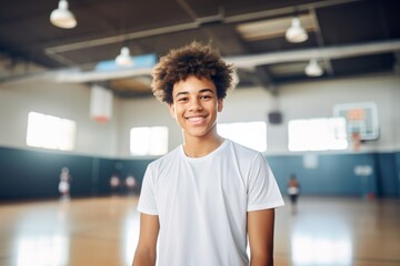 Smiling portrait of a teenage male African American basketball player wearing a white t shirt in an indoor basketball gym