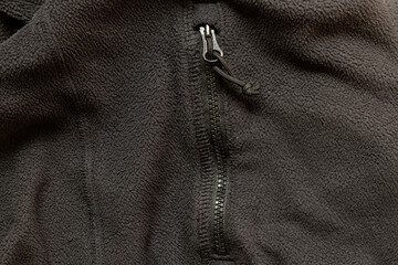 Texture of black fleece jacket with zipper on pocket close-up, fabric and fittings, zipper