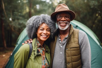 Fototapeta premium Portrait of a smiling african american senior couple infront of tent in forest during summer