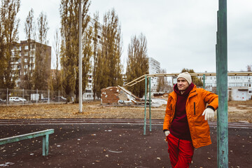 Obraz premium A young man wearing an orange jacket and red pants stands by a set of outdoor fitness bars, while enjoying the crisp autumn air and vibrant foliage.