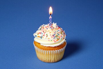 Vanilla cupcake with sprinkles and lit candle on blue background