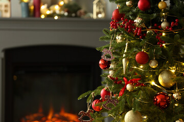 Beautiful decorated Christmas tree near fireplace at home, closeup. Space for text