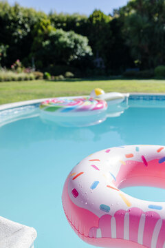 Pink sprinkled donut float is drifting on clear pool water near unicorn float in sunny backyard