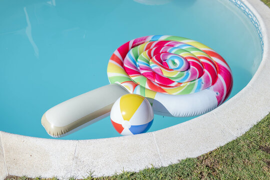 Colorful swirled lollipop-shaped float floating in backyard pool, featuring multicolored beach ball