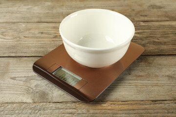 Electronic kitchen scale with empty bowl on wooden table, closeup